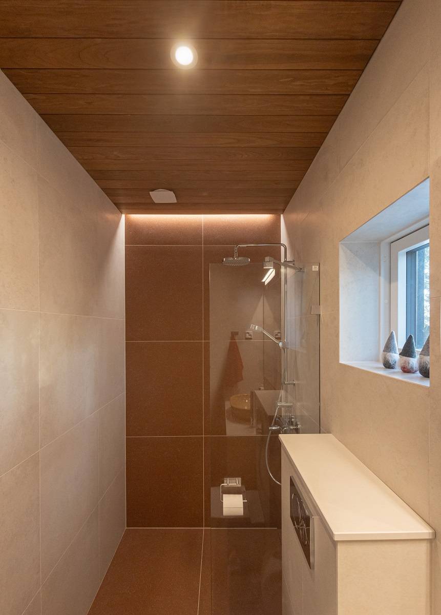 La pared trasera de la ducha se acentúa con una tira de iluminación LED uniforme y un foco empotrado como iluminación general.